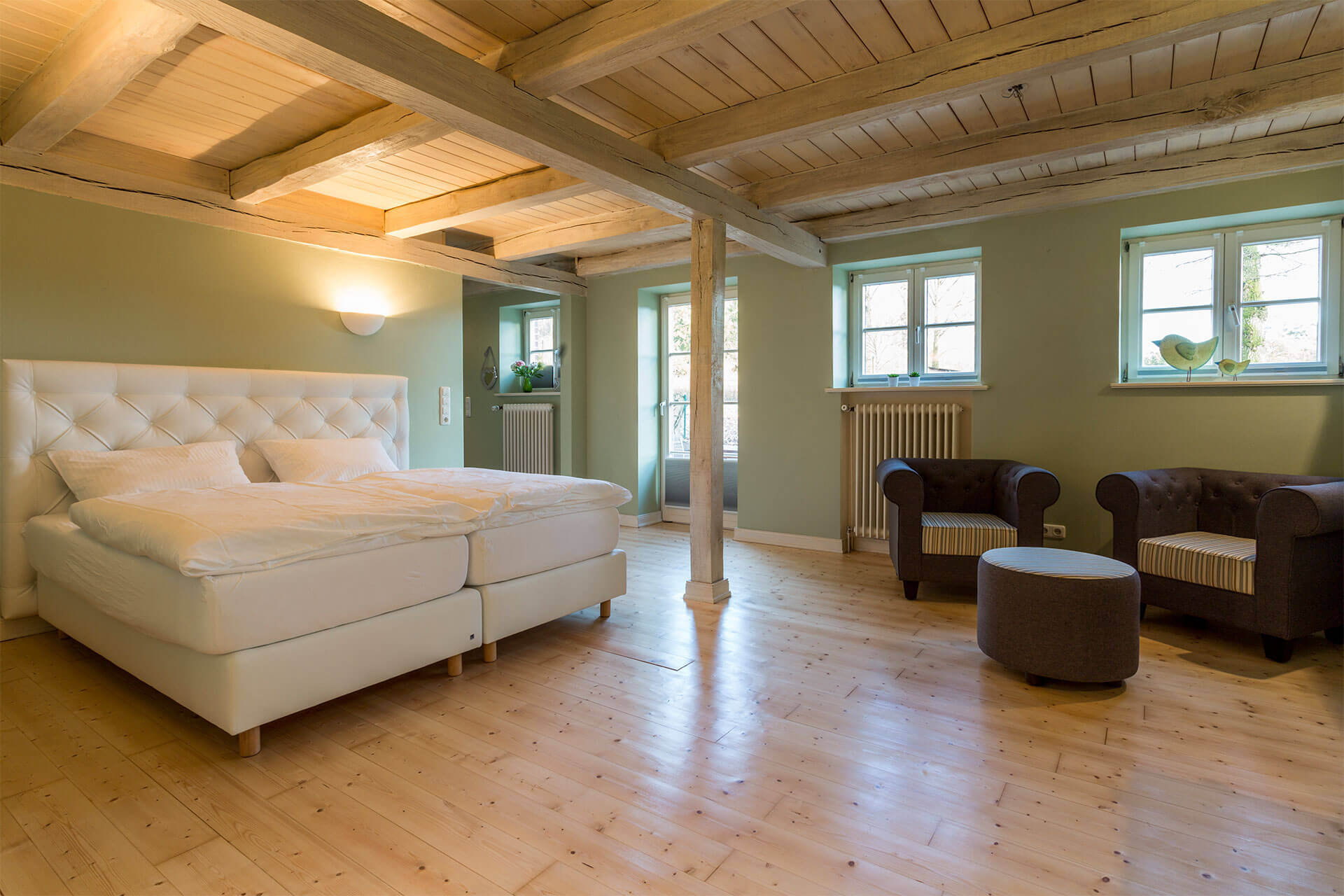 weißes Doppelbett auf Holzboden mit Sitzecke. Schön beleuchtet.